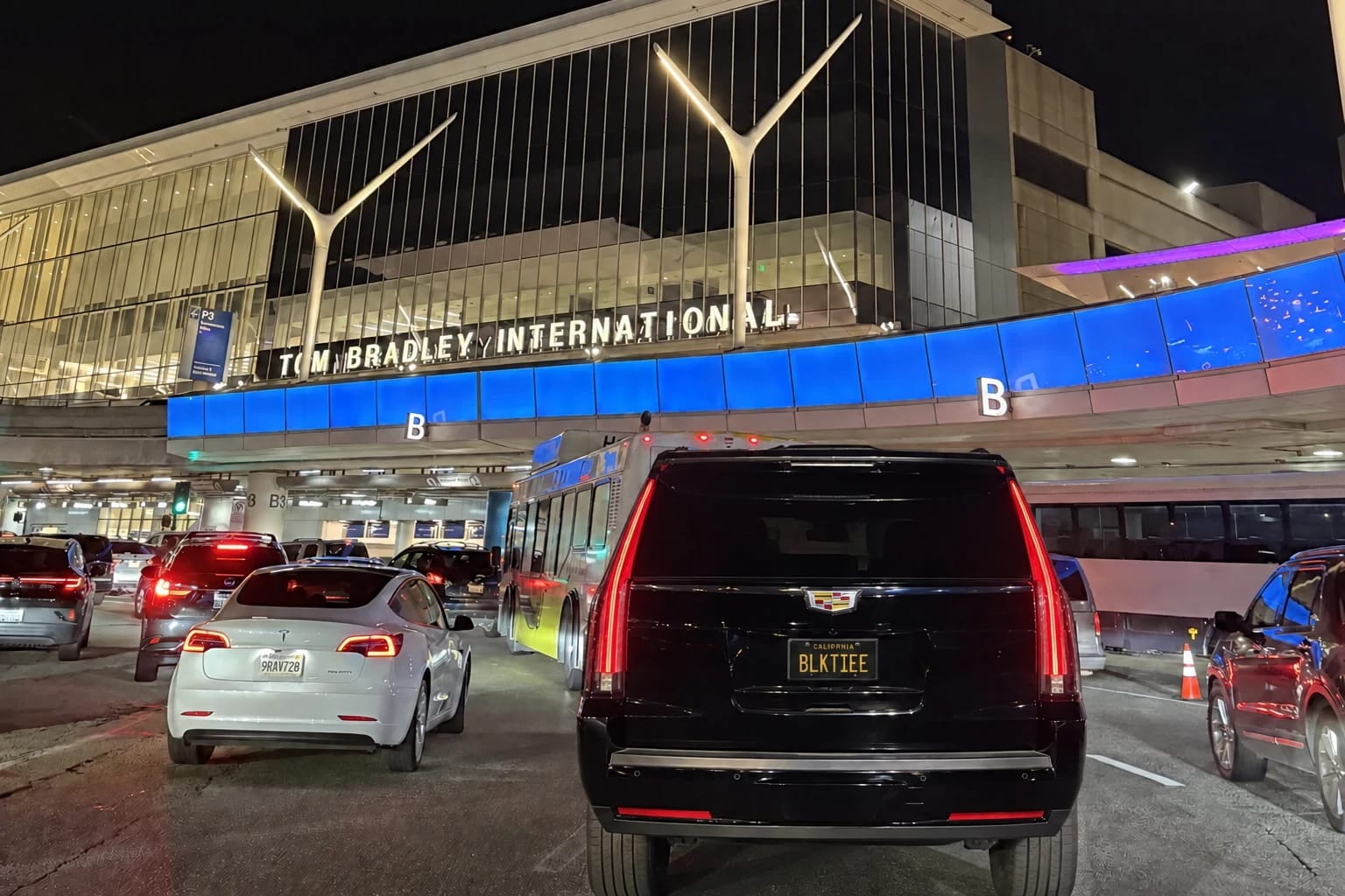 A black Cadillac Escalade waiting outside an airport terminal at night